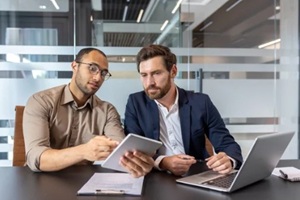 two businessmen reviewing a tablet and laptop