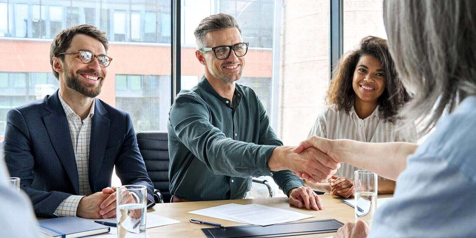 happy businessman and businesswoman shaking hands at group board meeting