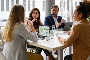 businesswoman reviewing report on her laptop while discussing business growth with coworkers in meeting