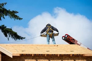 workman in safety harness on wood framed house roof carrying package of roofing materials delivered by conveyor belt on a sunny winter day